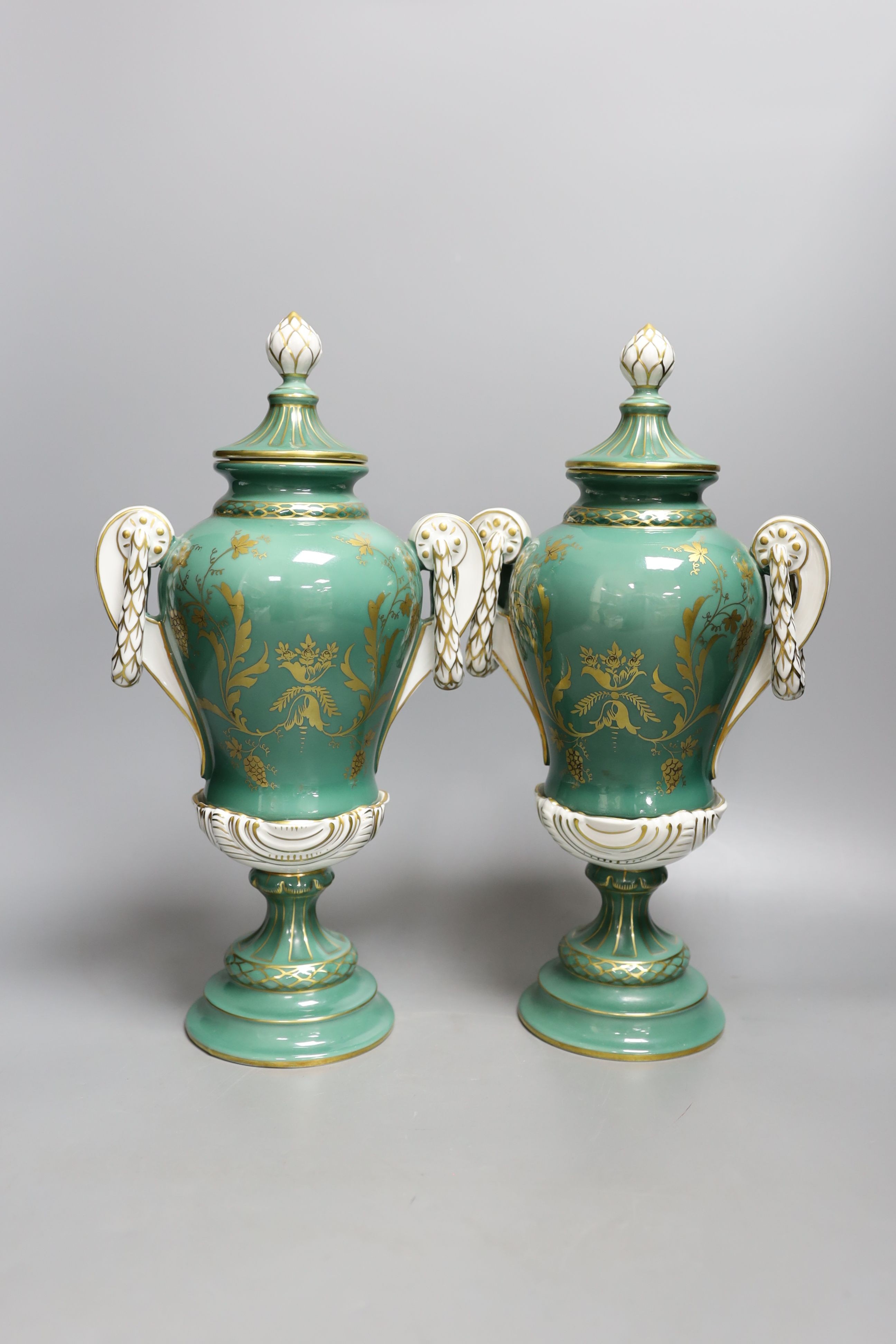 A pair of early 20th century Dresden vases painted with landscapes on an avocado green ground, 24cm high together with a German bottle vase and cover painted with four landscape panels separated by blue and white panels